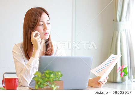 資料を見ながらこれはどうなっているの？と電話で話す女性 69908917