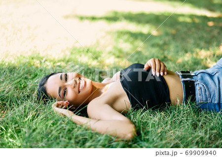 Portrait of pretty happy afro american woman relaxing on grass in park 69909940