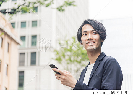 オフィス街でスマートフォンを操作する若い男性 オフィス街でスマートフォンを操作する若い男性 69911499