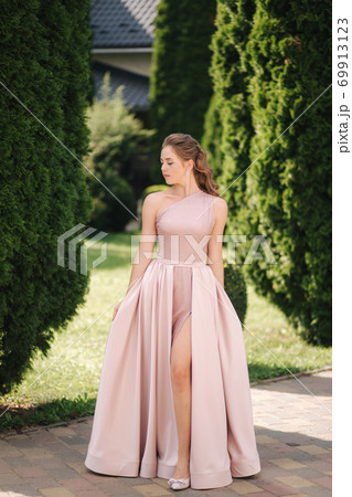 Beautiful young woman spin arround in gorgeous evening dress, background of green thee 69913123