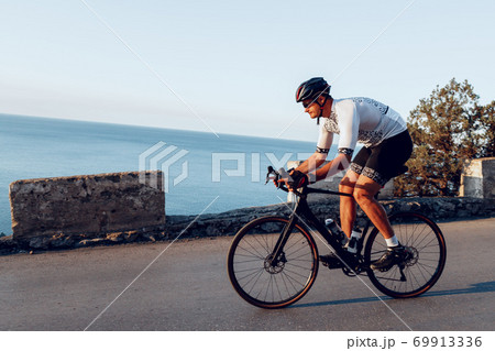 Man cyclist pedaling on a road bike outdoors in sun set 69913336