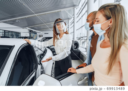 Woman car dealer consulting buyers wearing medical face shield 69913489