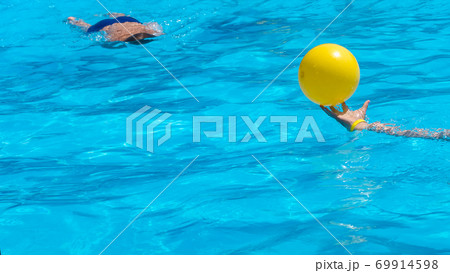Background In the pool, blurred figure of a diving boy and a hand holding a yellow ball  69914598
