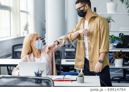 Contactless to say hello, health care and social distance during covid-19 pandemic. Young man and lady in protective masks greet with elbows 69914764
