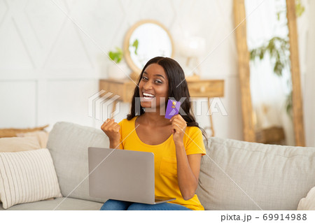 Online shopping. African American woman with laptop and credit card making YES gesture over big discount at home Online shopping. African American woman with laptop and credit card making YES gesture over big discount at home 69914988