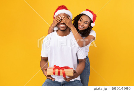 Black Girlfriend Congratulating Boyfriend On Christmas, Covering Eyes, Yellow Background Black Girlfriend Congratulating Boyfriend On Christmas, Covering Eyes, Yellow Background 69914990