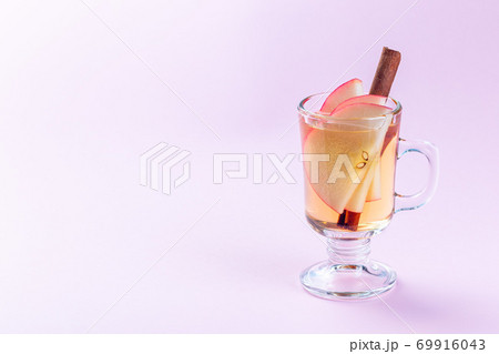 Glass of white glogg or mulled wine with apple slices and cinnamon stick on a pink background, horizontal, copy space 69916043