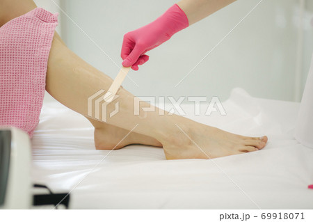 Young woman beautician in mask applies contact gel on the leg of a woman for laser hair removal in medical clinic. Close up. Pink glowes 69918071