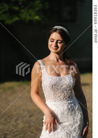 Elegant model in wedding dress posing to photographer outdoors. Beautiful young woman with fashion makeup 69918363