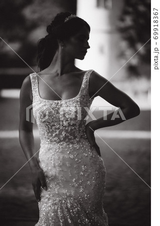 Elegant model in wedding dress posing to photographer outdoors. Beautiful young woman with fashion makeup 69918367