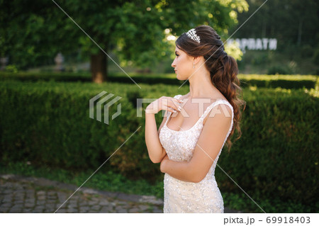 Elegant model in wedding dress posing to photographer outdoors. Beautiful young woman with fashion makeup 69918403