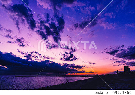 茜色に染まる黄昏時 静かな海に散歩する人影と遠くに見える東京スカイツリーが映える感動的な夕焼けの写真素材
