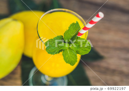 Juicy smoothie from mango in glass with striped red straw and with a mint leaf on old wooden background. Healthy life concept, copy space Juicy smoothie from mango in glass with striped red straw and with a mint leaf on old wooden background. Healthy life concept, copy space 69922197