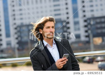 Modern confident young businessman in full suit standing outdoors with cityscape in the background 69928533