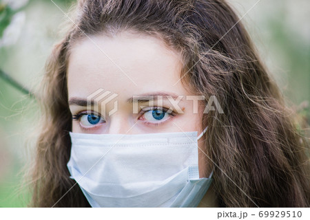 The girl with blue eyes in mask in blossom park. Covid -19 pandemic 69929510