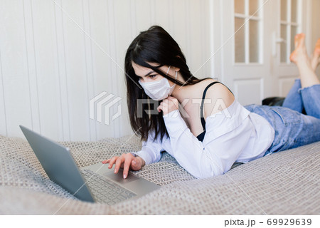 Beautiful female in quarantine wearing protective mask and working at home Beautiful female in quarantine wearing protective mask and working at home 69929639