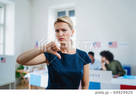 Portrait of serious woman voter with tumb down in polling place, usa elections concept. Portrait of serious woman voter with tumb down in polling place, usa elections concept. 69929920