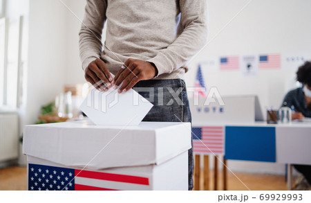 Unrecognizable african-american man putting his vote in the ballot box, usa elections and coronavirus. 69929993