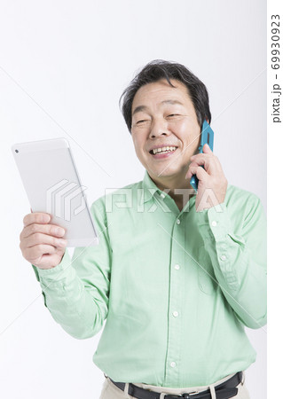 タブレットPCを見ながら電話をする男性 69930923