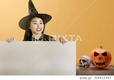 Asian witch woman with a hat standing with an empty board with a colored background Asian witch woman with a hat standing with an empty board with a colored background 69933305