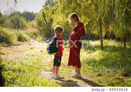 Small boy touching belly of his pregnant mother outdoors. 69933619