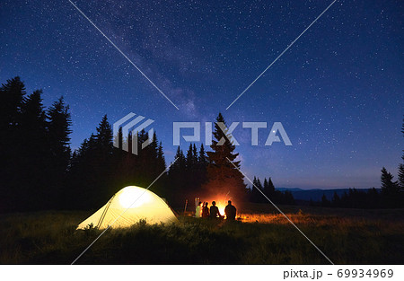 Tourists sitting near campfire under starry sky. 69934969