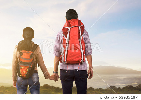 Rear view of Asian couple with backpack looking at mountain view Rear view of Asian couple with backpack looking at mountain view 69935187
