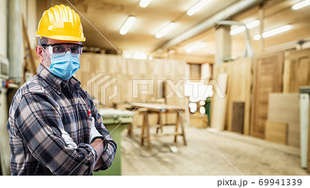 Carpenter at work protects the face with the surgical mask. Carpentry. Covid-19 prevention. 69941339