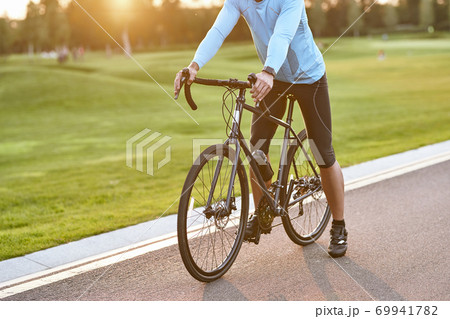 Getting ready to ride. Cropped shot of a road bicycle racer in sportswear standing on the road in park at sunset, cycling outdoors 69941782