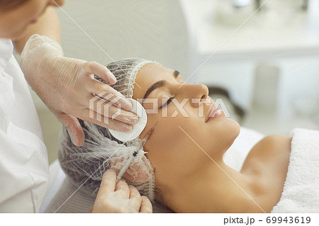 Cosmetologist wiping skin with cotton pads during facial beauty botox injection for young womans cheek Cosmetologist wiping skin with cotton pads during facial beauty botox injection for young womans cheek 69943619