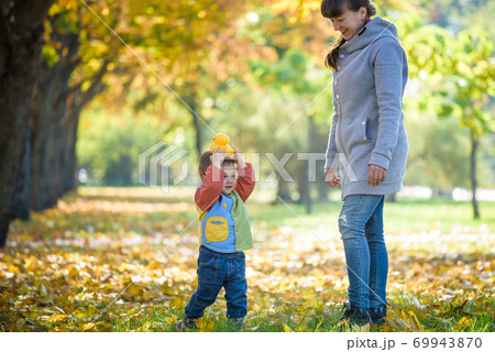 Happy young mother playing with baby in autumn park with yellow maple leaves .Family walking outdoors in autumn. Little boy with her mother playing in the park in autumn 69943870