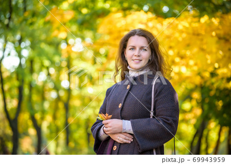 Young woman with autumn leaves in hand and fall yellow maple garden background 69943959