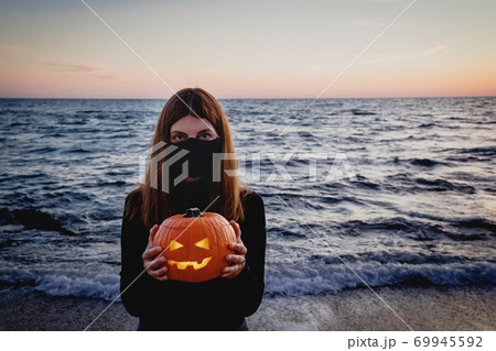 Woman wearing protective mask holding jack o lantern pumpkin Woman wearing protective mask holding jack o lantern pumpkin 69945592