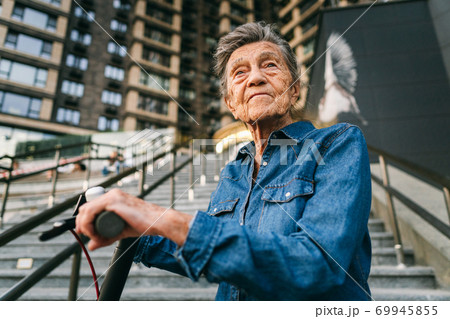 Active old woman riding electric scooter. Retired lady uses environmentally friendly city vehicle. Granny very old with gray hair, active and progressive. Modern senior woman use technology e scooter Active old woman riding electric scooter. Retired lady uses environmentally friendly city vehicle. Granny very old with gray hair, active and progressive. Modern senior woman use technology e scooter 69945855