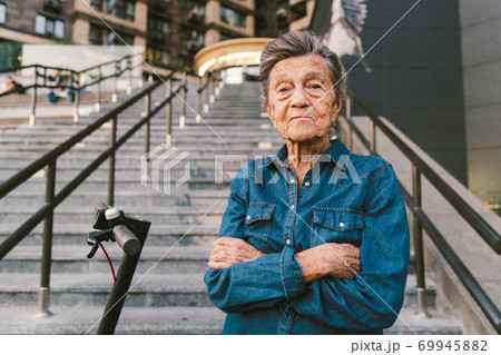 90 year old woman with gray hair, wrinkles, progressive and active uses modern electric transport scooter. Lady pensioner use eco friendly city vehicle. Senior female using urban personal transport 69945882