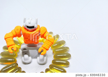 Fish oil capsules with orange toy robot made from rubber in the middle isolated on white background. 69946330