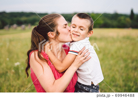 Mother and son hugging in field. Happy mother embracing her son in park. Mother hugging her child. Motherhood. Young mother cuddle her happy baby in fields at sunset. Lovely little kid 69946488