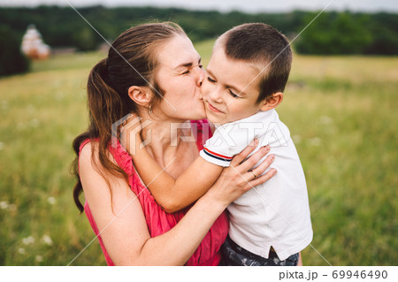 Young caucasian mother holds in her arms hugs and hugs her son in nature in summer. Motherhood and family happiness. A single mother and her child have fun together. Mom and son hugging 69946490
