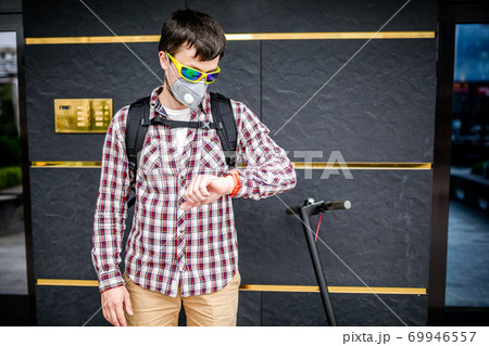 Male courier wearing protective face mask arrived at delivery address on electric scooter. Subject delivery during covid 19 on environmentally friendly transport. Pollution in big city. PM 2.5 mask 69946557