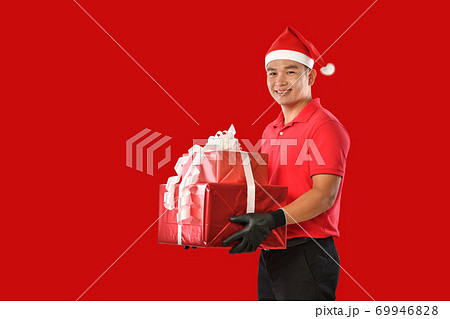 Delivery man in red uniform, face mask, protective gloves, Christmas hat carry boxes of presents  69946828