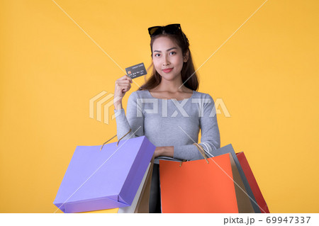 Young Asian woman with colourful shopping bags and credit card isolated on yellow background 69947337