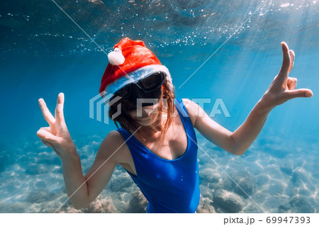 Happy freediver woman with New year cap glides underwater in blue ocean. Christmas holidays concept 69947393