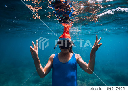 Happy freediver woman with New year cap glides underwater in blue ocean. Christmas holidays concept Happy freediver woman with New year cap glides underwater in blue ocean. Christmas holidays concept 69947406