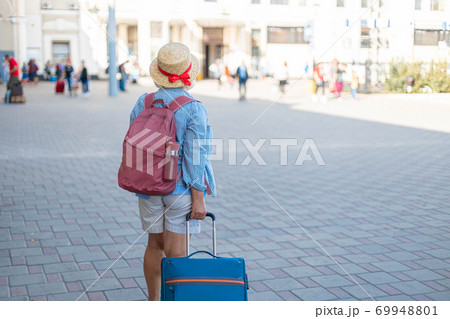 Woman traveler tourist in blue casual clothes, hat with backpack and carry-on luggage stands on the platform of the station. Woman traveler tourist in blue casual clothes, hat with backpack and carry-on luggage stands on the platform of the station. 69948801