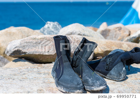 Dive boots drying on a stone. A dive flag and blue water in the background 69950771