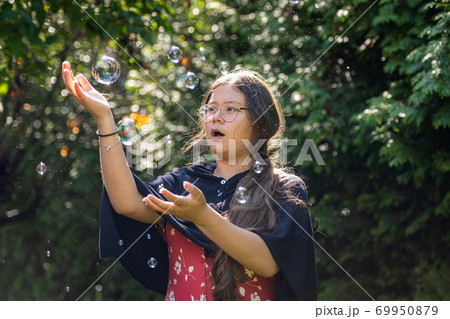 A preteen girl chasing soap bubbles. Green leaves background A preteen girl chasing soap bubbles. Green leaves background 69950879