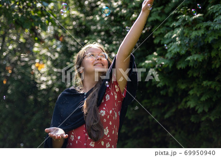 A preteen girl chasing soap bubbles. Green leaves background A preteen girl chasing soap bubbles. Green leaves background 69950940