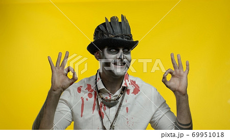 Sinister man with horrible Halloween skeleton makeupmaking faces, looking at camera, showing ok sign Sinister man with horrible Halloween skeleton makeupmaking faces, looking at camera, showing ok sign 69951018