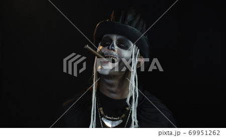 Frightening man in skeleton Halloween cosplay costume smoking cigar, making faces, smiling 69951262