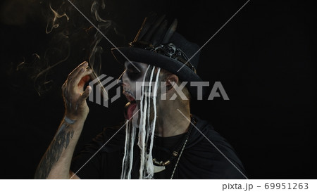 Scary guy in carnival costume of Halloween skeleton smoking cigar, making faces, showing tongue 69951263
